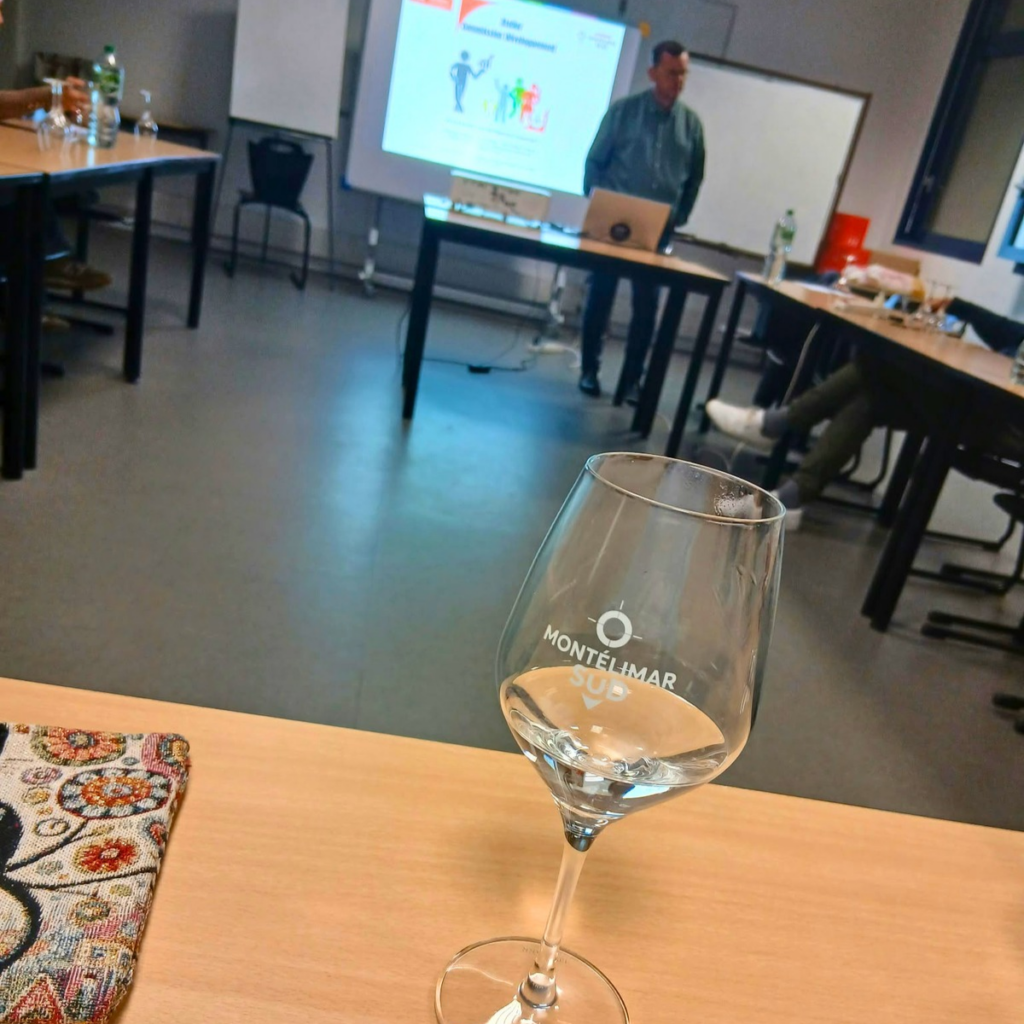 Verre au logo Montélimar Sud au premier plan, avec l’animateur et l’écran de présentation en arrière-plan.